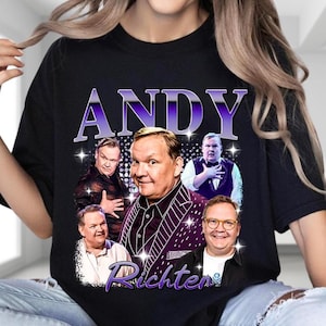 May include: Black t-shirt featuring a graphic of Andy Richter in various poses, with the name "ANDY" in purple letters at the top and "Richter" at the bottom. The design includes a vintage, retro style.