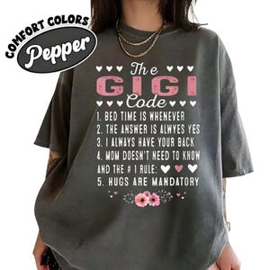 May include: Dark gray comfort colors t-shirt with the text "The Gigi Code" in pink and white. The shirt lists five rules, including "Hugs are mandatory." A floral design is at the bottom.