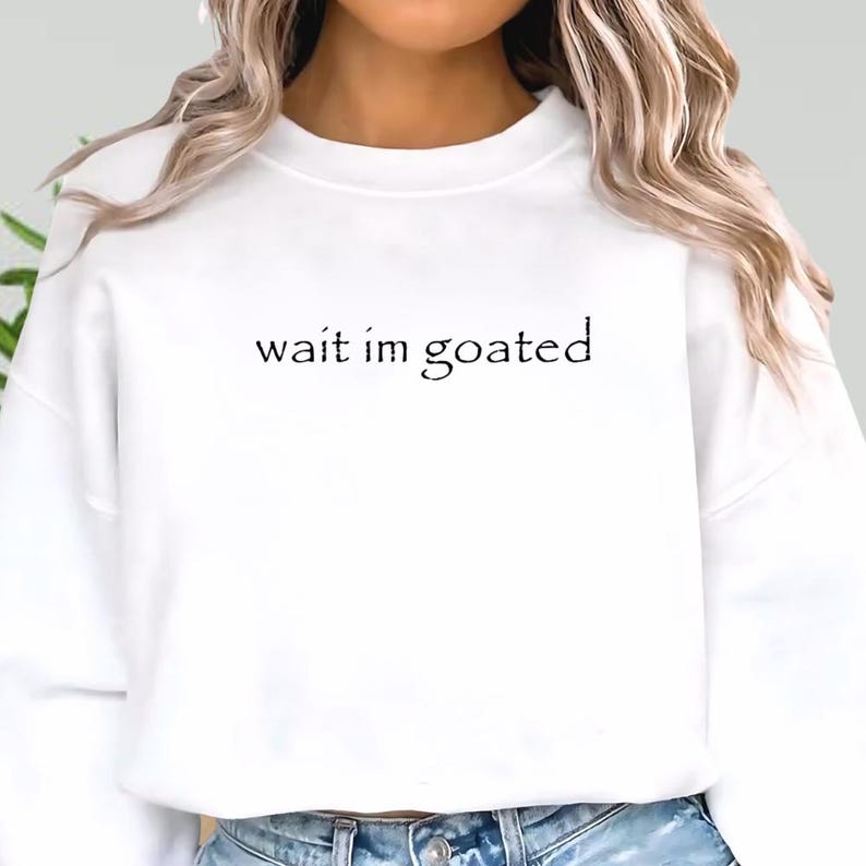 a woman wearing a white sweatshirt that says wait im goated