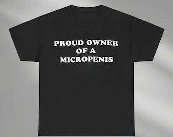 以下が含まれることがあります： 黒いTシャツ。白い文字で「PROUD OWNER OF A MICROPENIS」と太字のサンセリフ体で書かれています。Tシャツはクルーネックで、綿または同様の生地で作られているようです。テキストは胸の中央に配置されています。