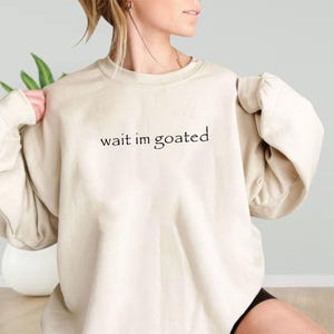 a woman wearing a sweatshirt that says wait i'm goated