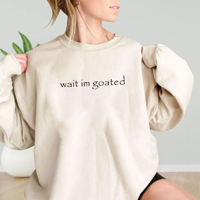 a woman wearing a sweatshirt that says wait i'm goated