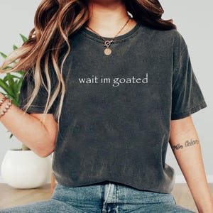 a woman wearing a t - shirt that says wait in goated