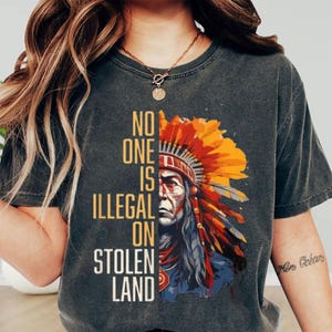 a woman wearing a t - shirt that says no one is illegal on stolen land