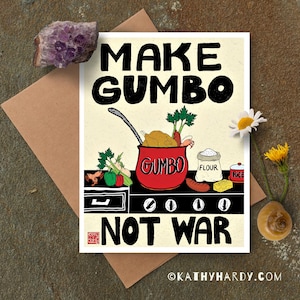 Puede incluir: Tarjeta con el texto "MAKE GUMBO NOT WAR" en negro. Muestra una olla roja de gumbo con ingredientes y una ilustración de cocina. Un cristal morado y flores se colocan cerca de la tarjeta.