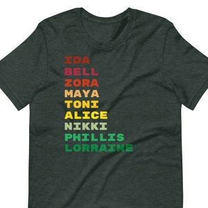 K&ouml;nnte beinhalten: Dunkelgr&uuml;nes T-Shirt mit einer vertikalen regenbogenfarbenen Grafik der Namen Ida Bell, Zora, Maya, Toni, Alice, Nikki, Phillis und Lorraine.