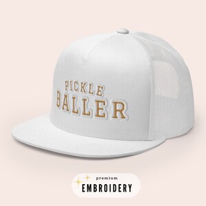 May include: White trucker hat with a brown embroidered design that says "Pickle Baller" with the words "premium embroidery" below the design.