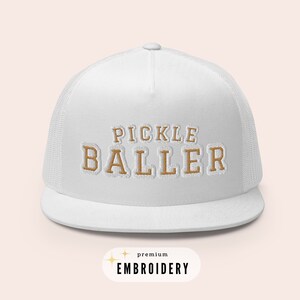 May include: White trucker hat with a gold embroidered design that says "Pickle Baller". The hat has a mesh back and a curved brim. The text "premium embroidery" is also visible in the image.