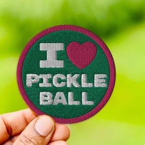 May include: A green and pink embroidered patch with the text "I love pickleball" in white lettering and a red heart.