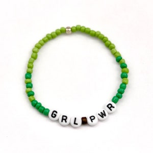 May include: Green beaded bracelet with the word "GRL PWR" spelled out in white beads.