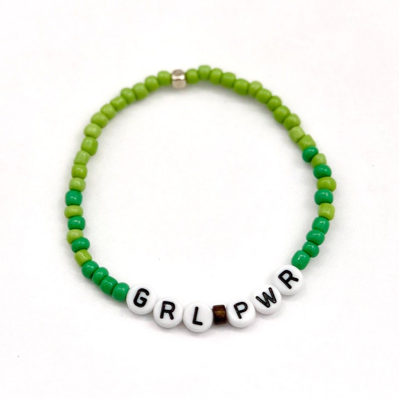 May include: Green beaded bracelet with the word "GRL PWR" spelled out in white beads.