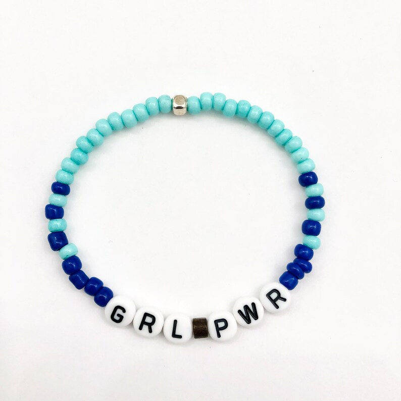 May include: A blue and light blue beaded bracelet with the word "GRL PWR" spelled out in white letters on white beads.