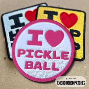 May include: A white and pink embroidered patch with the text "I love pickleball" in pink lettering. The patch is round and has a pink border. The patch is a premium embroidered patch.