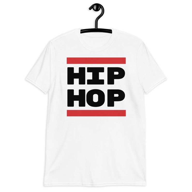 May include: White t-shirt featuring the words "HIP HOP" in bold black lettering, set between two red horizontal lines. The t-shirt is displayed on a black hanger.