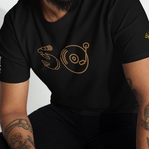 May include: A black t-shirt with a gold outline of a microphone and a record player. The text "EST. 2018" is on the right sleeve.