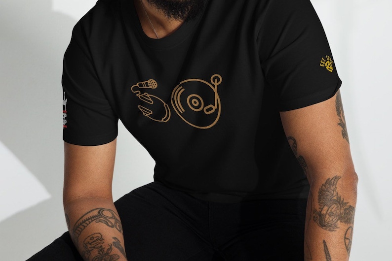 May include: A black t-shirt with a gold outline of a microphone and a record player. The text "EST. 2018" is on the right sleeve.