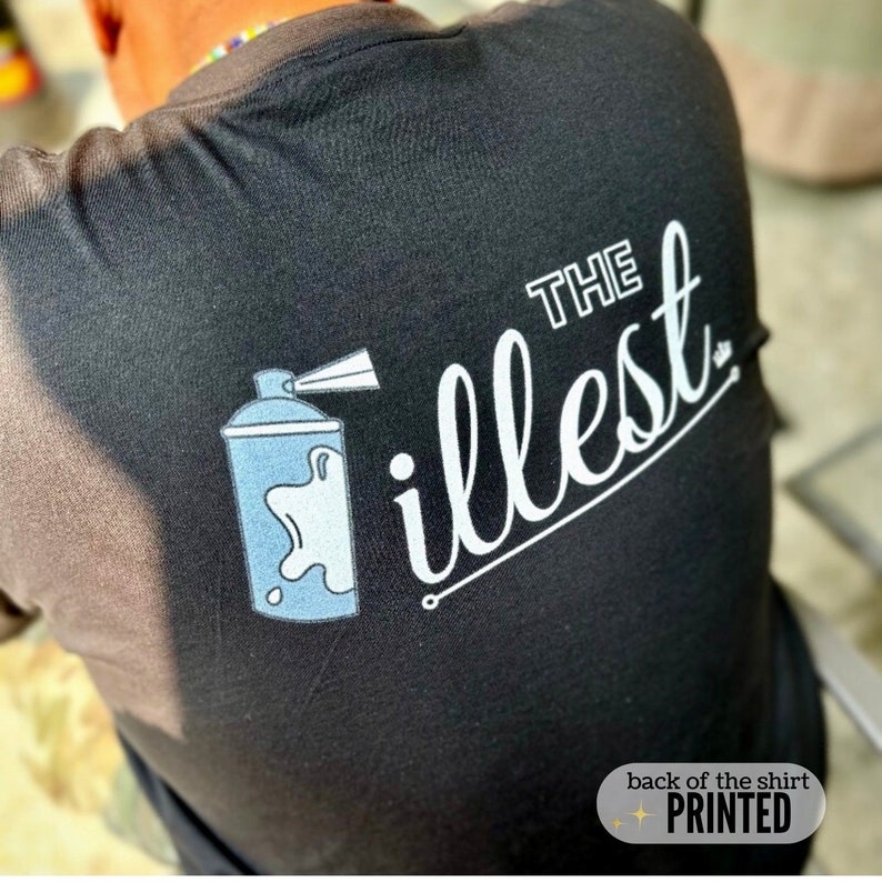May include: Black t-shirt with white text that says "THE illest" and a blue spray paint can graphic. The text is in a cursive font. The back of the shirt is printed.