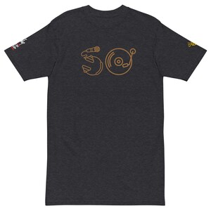 May include: A dark heather grey t-shirt with a gold outline of a microphone and a record player. The design is a stylized representation of the number 50.