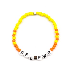 May include: A yellow and orange beaded bracelet with the letters "GRL PWR" spelled out in white beads.