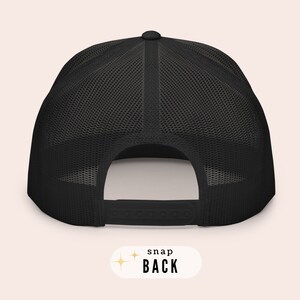 May include: Black mesh trucker hat with a black snap closure on the back. The hat has a black front panel and a mesh back panel.