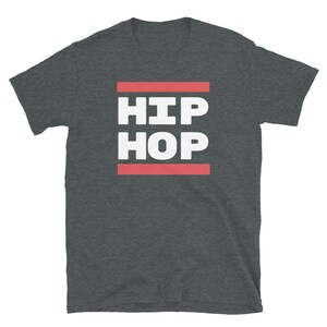 May include: Dark grey t-shirt featuring the words "HIP HOP" in white, bold capital letters, set between two red horizontal lines. The tee shirt has a crew neck and short sleeves.
