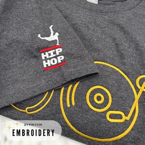 May include: A dark gray t-shirt with gold embroidery of a record player and the words "HIP HOP" in red and white embroidery.