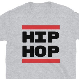 May include: A light grey t-shirt featuring the words "HIP HOP" in large, bold, black letters. The text is framed by two horizontal red lines. The shirt is made of a soft material.