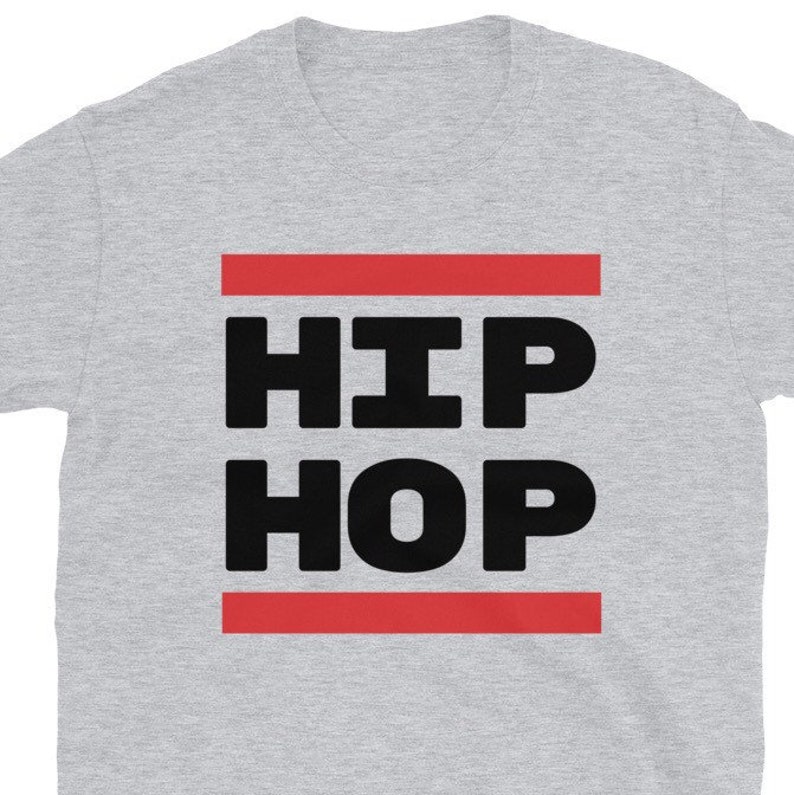 May include: A light grey t-shirt featuring the words "HIP HOP" in large, bold, black letters. The text is framed by two horizontal red lines. The shirt is made of a soft material.