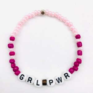 May include: Pink and magenta beaded bracelet with the word "GRL PWR" spelled out in white letters.