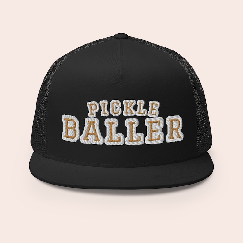 May include: Black trucker hat with a white mesh back. The hat has a gold embroidered design that says "Pickle Baller".