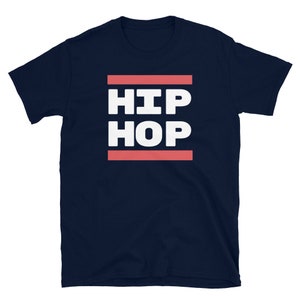 May include: A navy blue t-shirt featuring the text "HIP HOP" in bold white capital letters, set between two coral-coloured lines. The shirt has a crew neck and short sleeves.