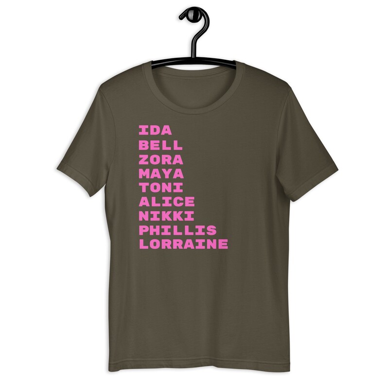 K&ouml;nnte beinhalten: Ein dunkelbraunes T-Shirt mit einer vertikalen Liste von Namen in Pink gedruckt: Ida, Bell, Zora, Maya, Toni, Alice, Nikki, Phillis, Lorraine.