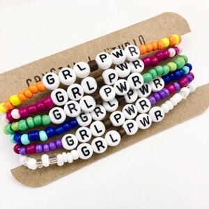 May include: Set of six colorful beaded bracelets with white beads that spell out "GRL PWR".