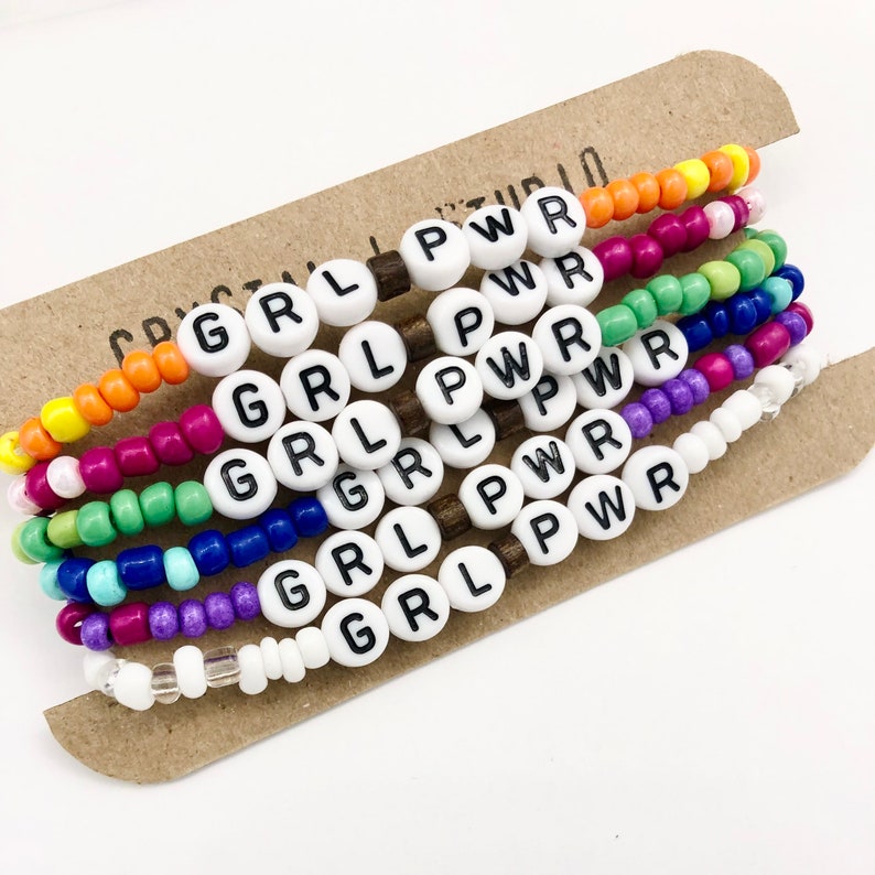 May include: Set of six colorful beaded bracelets with white beads that spell out "GRL PWR".