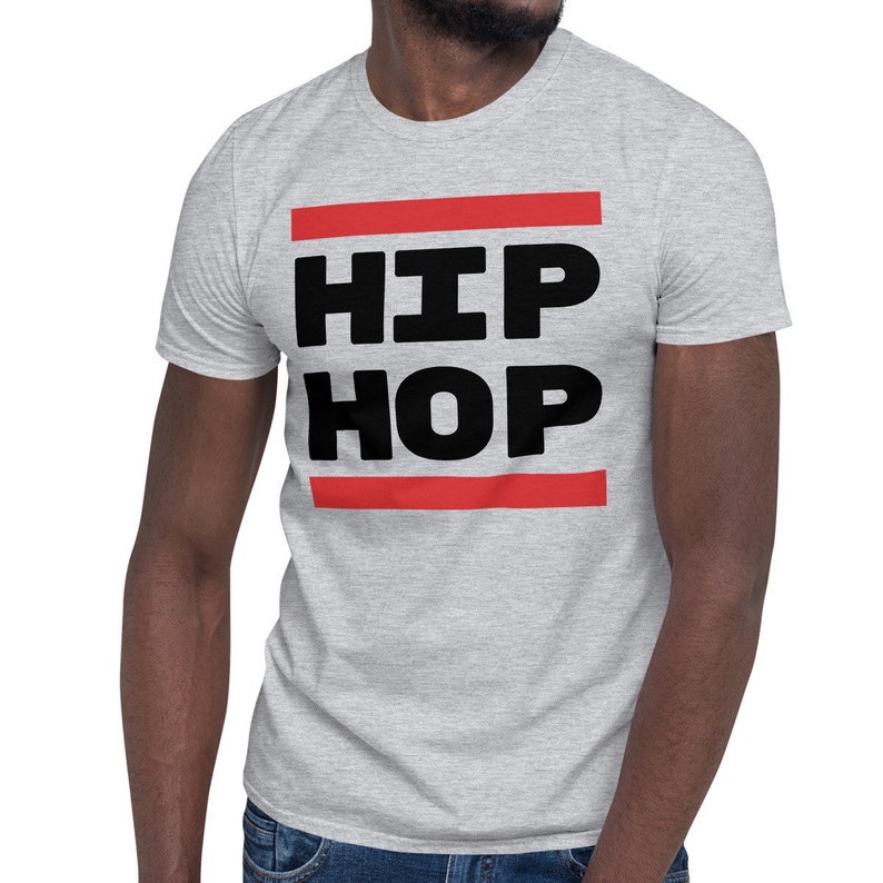 May include: A light grey t-shirt featuring the words "HIP HOP" in bold black lettering, set between two red horizontal lines. The shirt is short-sleeved and made of a soft fabric.