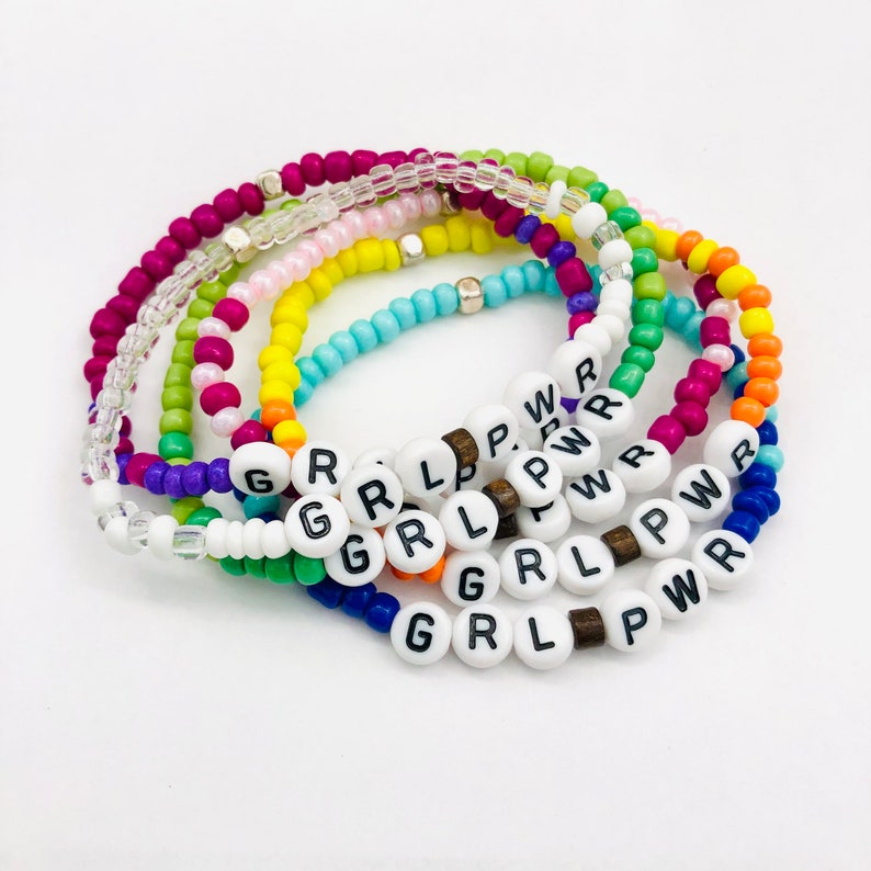 May include: A set of colorful beaded bracelets with white beads that spell out "GRL PWR".