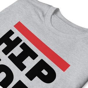 May include: A light grey t-shirt with the word "HIP" in large, bold, black letters, with "HOP" below. A thick red line slashes diagonally across the text. The shirt has a crew neck.