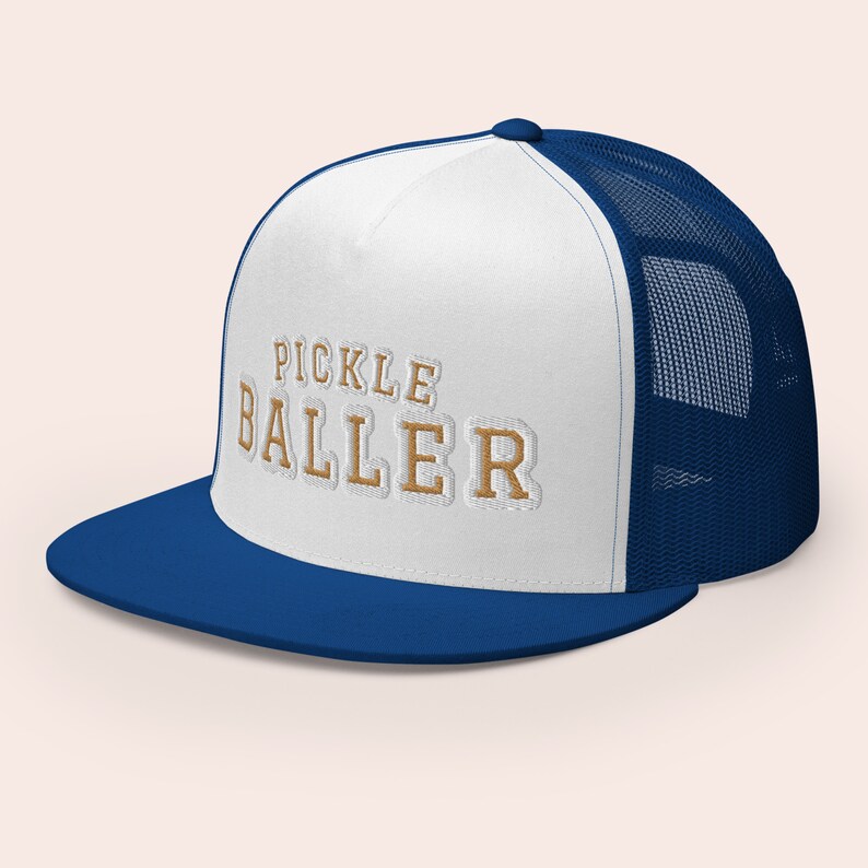 May include: A white and blue trucker hat with a mesh back. The front of the hat has the text "PICKLE BALLER" in gold embroidery.