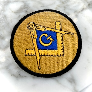 May include: A gold and blue embroidered patch with a compass and square, a symbol of Freemasonry.