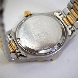 Pu&ograve; includere: Primo piano del retro di un orologio da polso argentato e dorato. Il quadrante dell'orologio &egrave; rotondo con finitura argentata e il marchio "HEUER" &egrave; visibile. Il cinturino &egrave; una combinazione di maglie argentate e dorate.