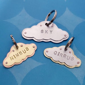 May include: Three metal cloud-shaped keychains with different names: "SKY", "NIMBUS", and "CIRRUS". The keychains are silver, gold, and copper.