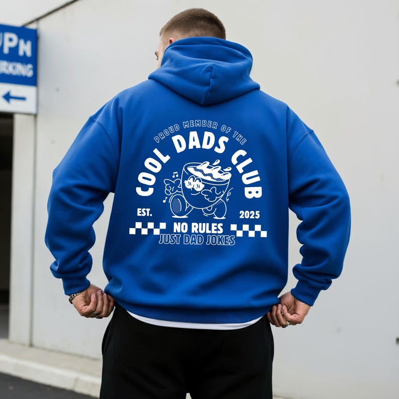 May include: A vibrant blue hoodie featuring a white graphic on the back. The design includes the text "COOL DADS CLUB" and a cartoon bowl character. The phrase "NO RULES JUST DAD JOKES" is also printed on the hoodie.