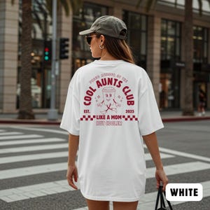 May include: White t-shirt with a maroon graphic on the back that reads "COOL AUNTS CLUB" with a cartoon coffee cup character. The text "EST. 2025" and "LIKE A MOM BUT COOLER" are also printed on the shirt. The word "WHITE" is printed on the bottom right.