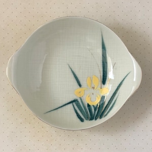 May include: A small, white ceramic bowl with a yellow flower and green leaves design. The bowl has two handles on the sides.