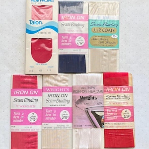 May include: A collection of vintage sewing notions, including Talon hem facing, iron-on seam binding, and hem tape. The packages feature text and graphics in various colors, including red, pink, blue, and white. The products are designed for sewing and garment construction.