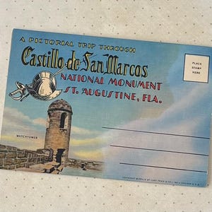 May include: Vintage postcard featuring a pictorial trip through Castillo de San Marcos National Monument in St. Augustine, Florida. The postcard has a blue sky background with an illustration of the watchtower and a sword and helmet.