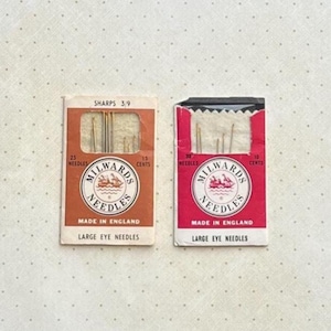May include: Two vintage needle packets. One is orange and the other is red. Both packets have the "Milwards Needles" logo and text that reads "Made in England" and "Large Eye Needles". The orange packet says "Sharps 3/9" and "25 Needles". The red packet says "30 Needles".