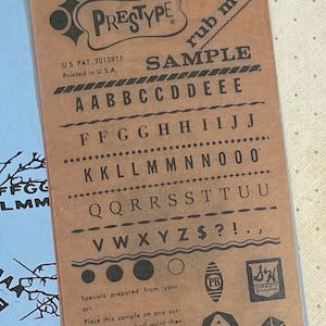 May include: A brown paper card with the text "PRESTYPE" and "rub me!" in black lettering. The card features a sample alphabet and special characters, including a dollar sign, question mark, exclamation point, and period. The text "SAMPLE" is printed in black lettering with a black border. The text "U.S. PAT. 3013917" and "Printed in U.S.A." is printed in black lettering. The card also includes instructions for using the sample.