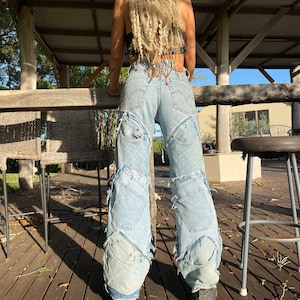 May include: A pair of light blue denim jeans with multiple patches and frayed edges. The jeans are worn by a person with long blonde hair.