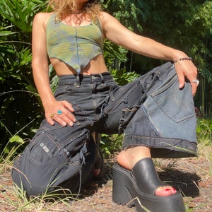 May include: A person wearing black denim pants with distressed details and a green and blue tie-dye crop top. The pants have multiple layers of denim and are ripped and frayed. The person is wearing black platform sandals.
